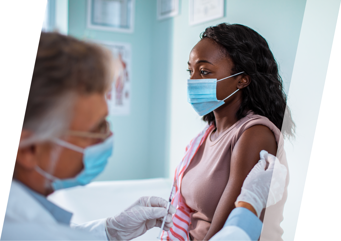 A male doctor wearing a mask giving a shot to an African American female patient.  